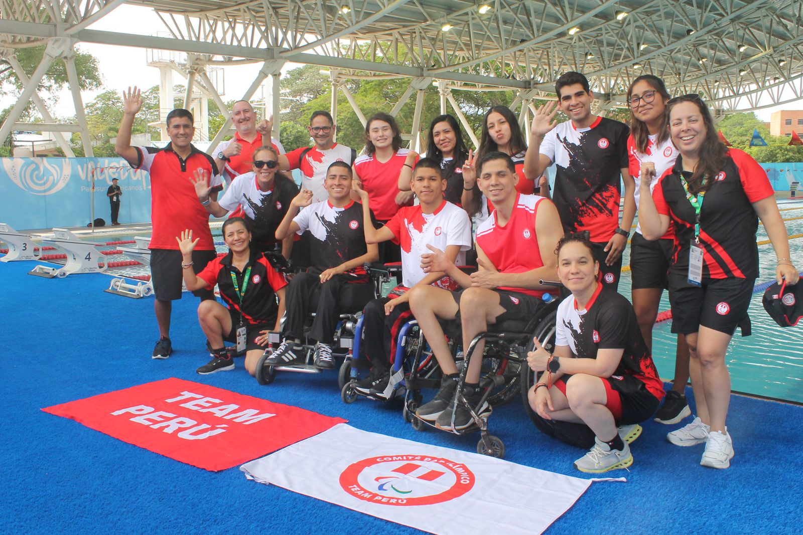 Delegación del Team Perú junto a la piscina, con para atletas en silla de ruedas y banderas del Comité Paralímpico del Perú